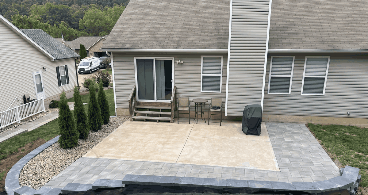 A detailed view of a newly landscaped backyard, showcasing a prominent row of conical arborvitae trees planted within a light-colored gravel bed.