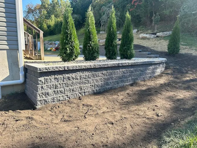 Curved segmental retaining wall with caps and arborvitae beside a patio in Valley Park, MO